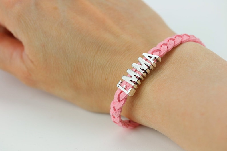 May include: A pink braided leather bracelet with a silver charm that says "EMMA".