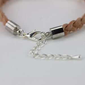 May include: A close-up of a light brown braided leather bracelet with silver metal end caps and a silver lobster clasp.