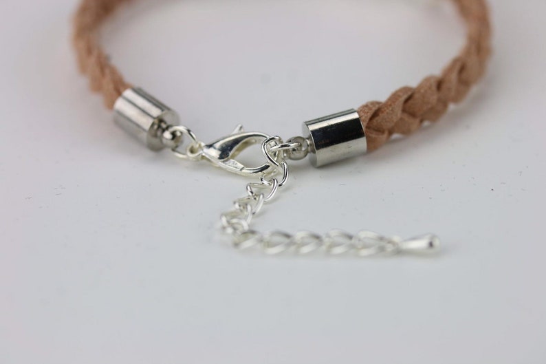 May include: A close-up of a light brown braided leather bracelet with silver metal end caps and a silver lobster clasp.