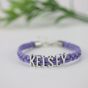 May include: A purple braided cord bracelet with the name "Kelsey" spelled out in silver letters.