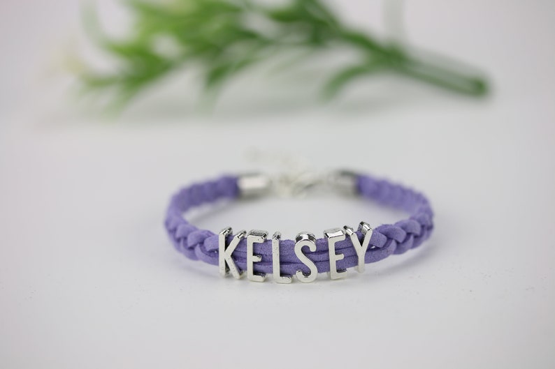 May include: A purple braided cord bracelet with the name "Kelsey" spelled out in silver letters.