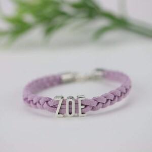 May include: A purple braided bracelet with a silver charm that says "ZOE".