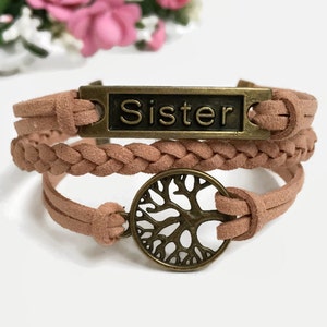 May include: A brown leather bracelet with a braided design and a metal charm that says "Sister" and a tree of life charm.