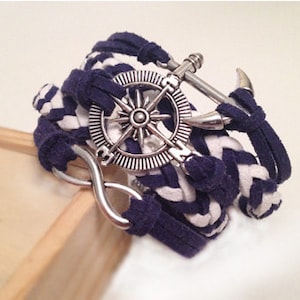 May include: A navy blue and white braided bracelet with a silver compass charm, an anchor charm, and an infinity symbol charm.