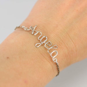 May include: A silver wire bracelet with the name "Angela" spelled out in cursive.