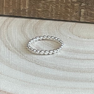May include: A silver beaded ring with a simple design. The ring is made of small, round beads that are evenly spaced.