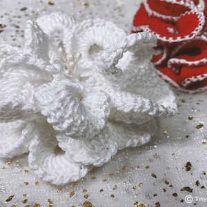May include: A white crocheted flower with a pearl center, on a white background with gold glitter.