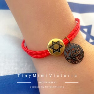 May include: Red string bracelet with a gold star of David charm and a black charm with Hebrew writing.