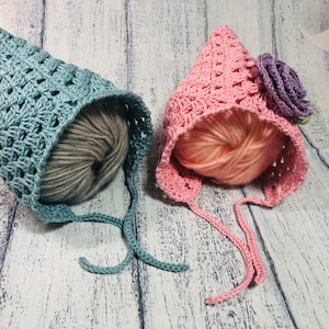 May include: Two crocheted baby hats, one light blue and one pink, with matching yarn balls. The pink hat has a purple flower embellishment.