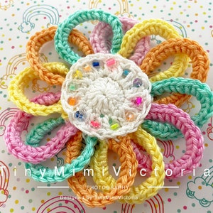 Peut inclure: Une fleur en crochet colorée avec un centre blanc et des pétales aux couleurs de l'arc-en-ciel. Le centre de la fleur est décoré de perles colorées.