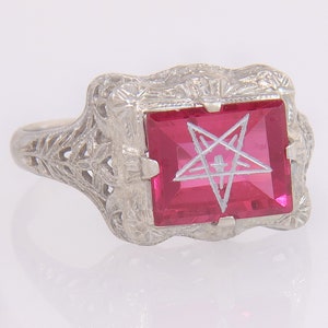 May include: A vintage silver ring with a large, square, ruby-red gemstone. The gemstone features a white pentagram design. The ring has an ornate, filigree design on the band and around the gemstone setting.