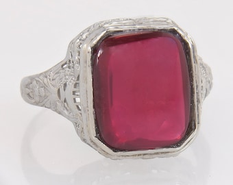 May include: A vintage silver ring with a rectangular, deep red gemstone. The ring features intricate filigree detailing on the band and around the gemstone setting. The gemstone is a vibrant, saturated red color, set in a detailed, ornate frame.