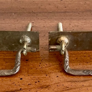 May include: Two antique brass drawer pulls with ornate designs. Each pull has a rectangular plate with a decorative handle.