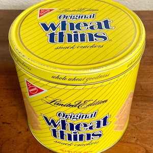 May include: A yellow, cylindrical tin of "Original Wheat Thins" snack crackers. The tin features blue text and a red Nabisco logo. The words "Limited Edition" and "whole wheat goodness" are also visible.