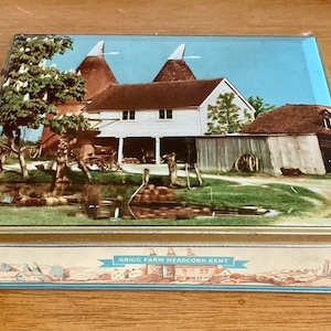 May include: A rectangular tin box with a scenic image of a farm with two conical structures, a white house, and a pond. The box has a blue and white border and the text "GRIGG FARM HEADCORN KENT".