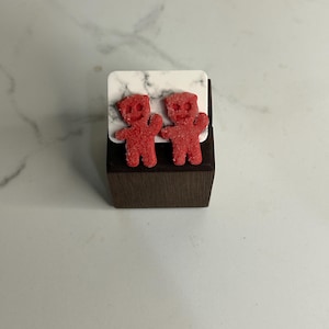 May include: A pair of red gummy bear stud earrings on a small wooden display stand.