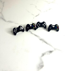 May include: Four black plastic game controller earrings with white and colored buttons.