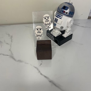 May include: Two white ceramic Star Wars Stormtrooper earrings on a display stand with a Star Wars R2-D2 toy in the background.