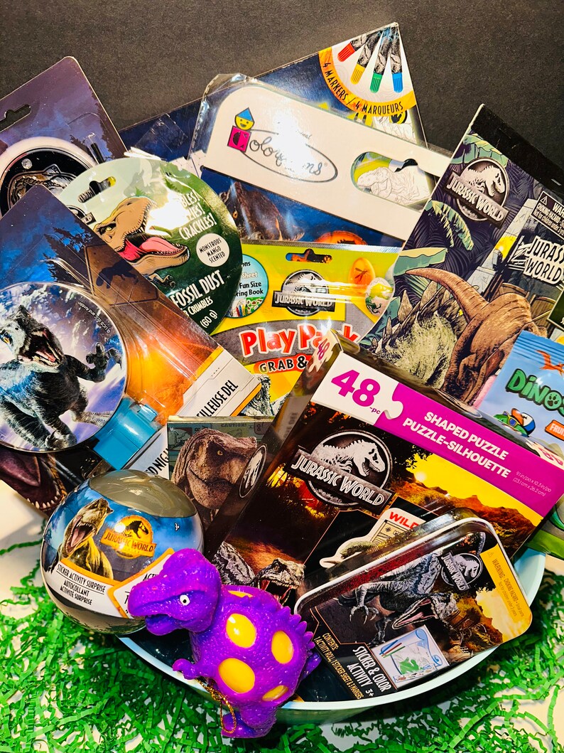 May include: A gift basket filled with Jurassic World themed toys and activities. The basket includes a dinosaur shaped stress ball, a sticker activity surprise, a shaped puzzle, a play pack, a coloring book, and a sticker and color activity book.