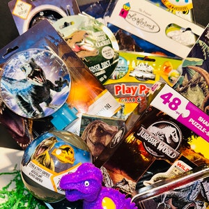 May include: A gift basket filled with dinosaur-themed toys and activities. The basket includes a purple dinosaur toy, a Jurassic World sticker activity, a dinosaur puzzle, and a dinosaur-shaped play dough set.