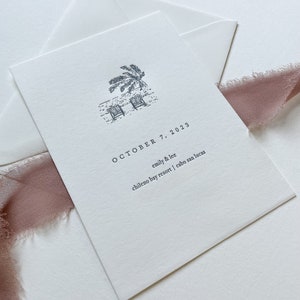 May include: A white invitation card with a beach scene illustration, palm tree, and two beach chairs. The text "OCTOBER 7, 2023" is printed above the names "emily & lee" and the location "chileno bay resort | cabo san lucas".