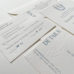 May include: Elegant wedding invitation suite in cream with blue text. Includes RSVP, details, and invitation cards. Floral and botanical design elements are embossed on the cards. The suite includes an envelope.