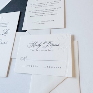 May include: A close-up of elegant wedding stationery. The image features a white RSVP card with embossed palm tree details and the words "Kindly Respond" in a decorative font. Other cards with text are also visible.