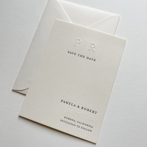 May include: Ivory-colored "Save the Date" card with matching envelope. The card features embossed initials "PIR" above the text "SAVE THE DATE." Below, it reads "PAMELA & ROBERT" and the date "10.07.23," followed by location and "INVITATION TO FOLLOW."