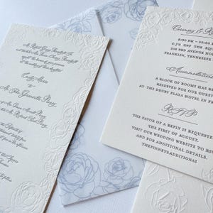 May include: A white wedding invitation with blue floral accents. The invitation includes the names "Emily Marie" and "Mr. The Granville Perry" and the date and time of the ceremony. The invitation also includes information about the reception and accommodations.