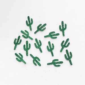 May include: A collection of green glitter cactus shapes on a white background.