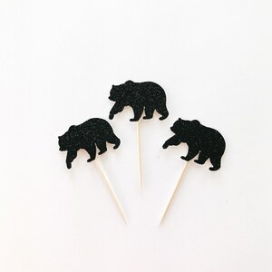 May include: Three black glitter bear cupcake toppers on white sticks. The bears are walking in a silhouette style.