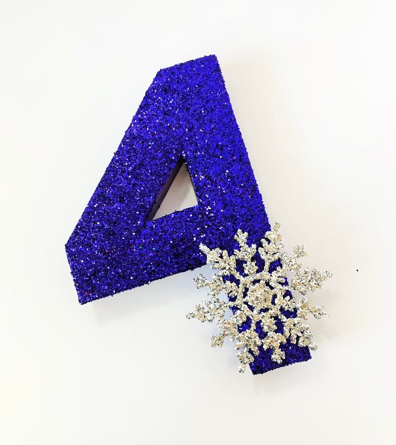 Pode incluir: Um n&uacute;mero quatro de glitter azul com uma decora&ccedil;&atilde;o de floco de neve de glitter prateado.