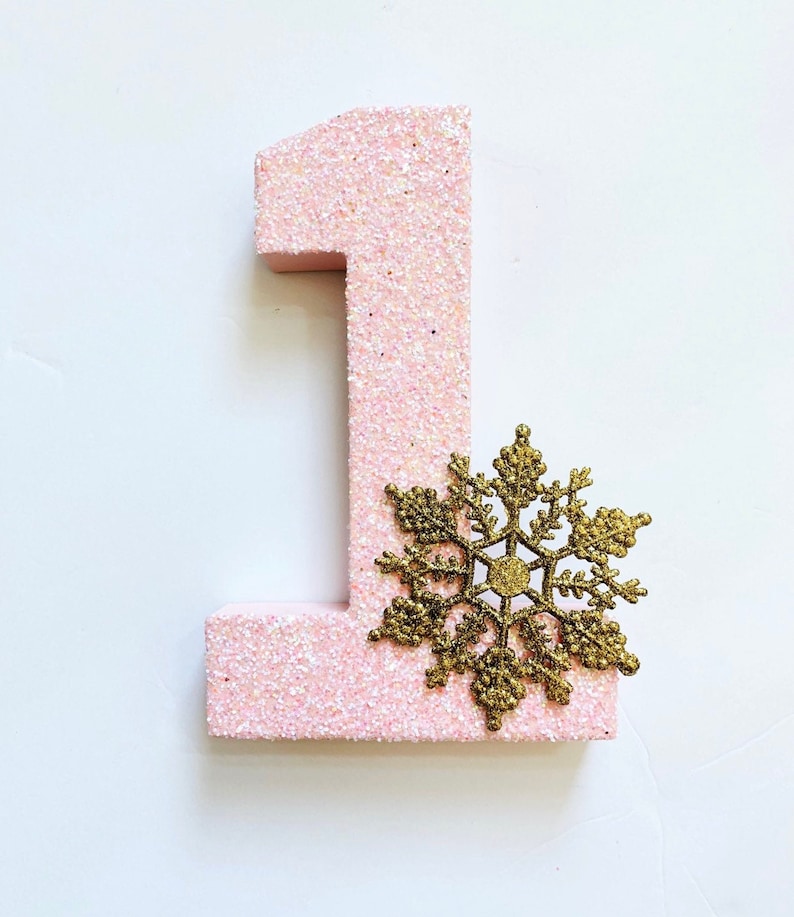 Pode incluir: N&uacute;mero um de glitter rosa com uma decora&ccedil;&atilde;o de floco de neve de glitter dourado.