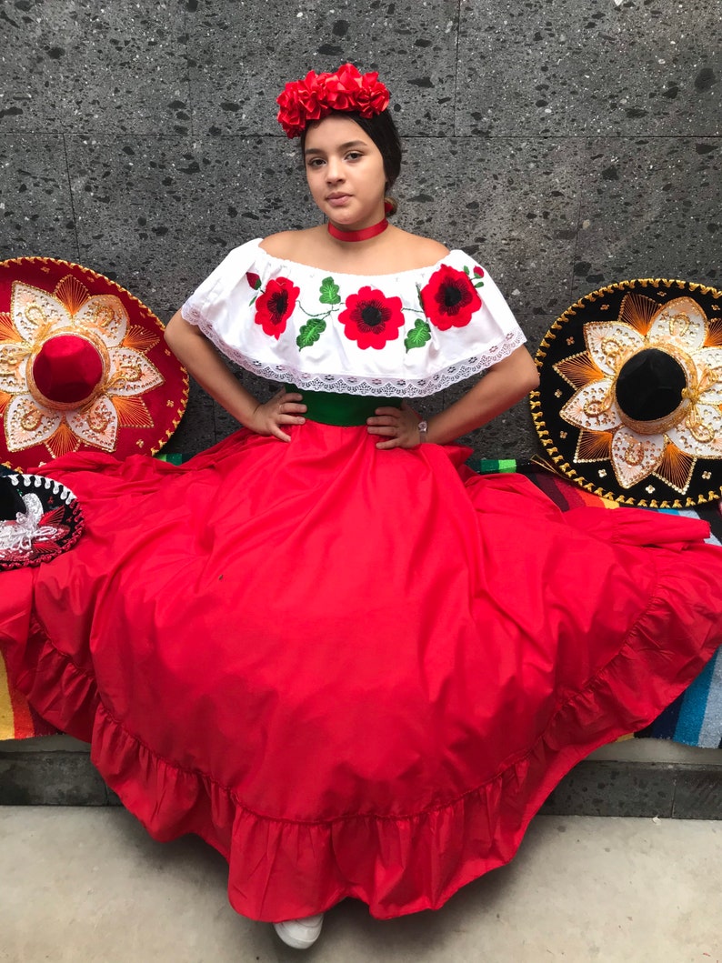 May include: A white off-the-shoulder blouse with red poppy embroidery and lace trim, paired with a long red skirt featuring a green waistband. The outfit includes a red fabric flower headpiece and a matching red choker, with two large sombreros nearby.
