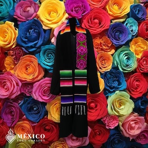 May include: A black garment with a colorful embroidered sash, set against a backdrop of vibrant roses in various colors. The sash features floral and striped patterns in shades of pink, green, orange, and purple. The image includes the text "MÉXICO TODO CORAZÓN".
