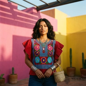 Puede incluir: Una blusa azul con mangas de volantes rojas y bordados florales vibrantes en rosa, morado y turquesa. La prenda presenta un escote cuadrado y se combina con un collar llamativo de plata y brazaletes anchos de plata en cada muñeca.