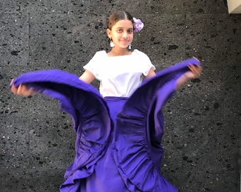 May include: A young person wearing a white blouse and a purple ruffled skirt. The skirt is gathered at the waist and has multiple layers of ruffles. The person is smiling and holding the skirt out to the sides.