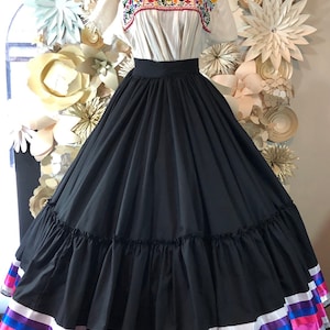 May include: A black skirt with multiple layers and a white ruffle trim. The skirt has a wide waistband and is decorated with colorful ribbon trim at the hem.