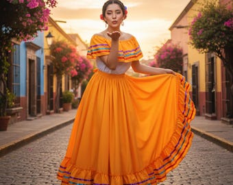 May include: A woman in a traditional Mexican dress, posing outdoors. The dress is bright orange with colorful trim. The off-the-shoulder top has a white base with a yellow and rainbow trim. The long skirt has a ruffled hem.