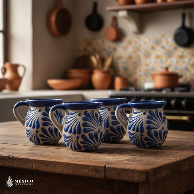 Peut inclure: Quatre tasses en c&eacute;ramique avec une base cr&egrave;me et un motif floral bleu sont pos&eacute;es sur une table en bois. Les tasses ont un bord et une anse bleus. L'arri&egrave;re-plan montre une cuisine avec des pots et des casseroles en terre cuite.