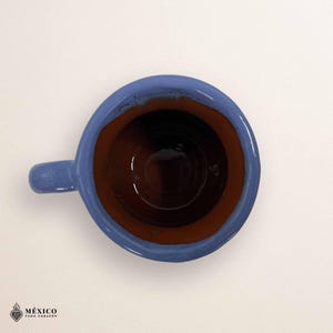 Peut inclure: Vue de dessus d'une tasse en c&eacute;ramique faite &agrave; la main, bleue et marron, avec une petite anse. L'int&eacute;rieur est brun fonc&eacute;, contrastant avec le bord et l'anse bleus. La tasse est probablement pour les boissons chaudes.