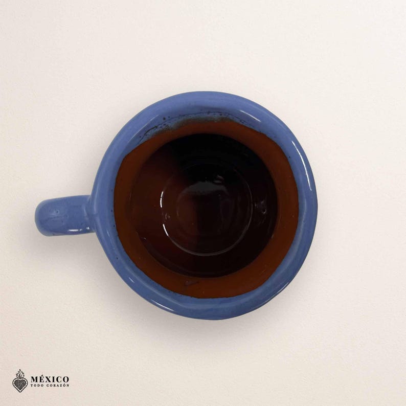 Peut inclure: Vue de dessus d'une tasse en c&eacute;ramique faite &agrave; la main, bleue et marron, avec une petite anse. L'int&eacute;rieur est brun fonc&eacute;, contrastant avec le bord et l'anse bleus. La tasse est probablement pour les boissons chaudes.