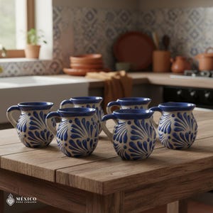 Peut inclure: Six tasses en c&eacute;ramique avec des motifs floraux bleus et blancs sont dispos&eacute;es sur une table en bois. Les tasses ont des anses et un bord bleu. L'arri&egrave;re-plan montre une cuisine avec d'autres articles en c&eacute;ramique.