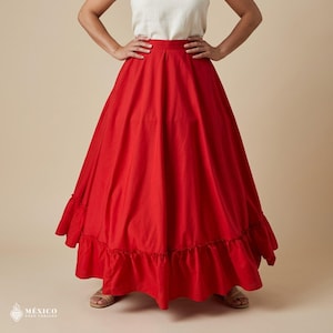 May include: A floor-length, solid red skirt featuring a high waistband and a wide, gathered ruffle detail along the bottom hem. The skirt is paired with a plain, short-sleeved white top. The text "M&Eacute;XICO TODO CORAZ&Oacute;N" is visible in the bottom corner.