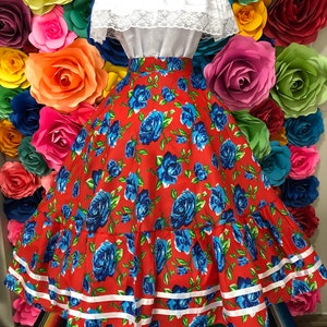 Puede incluir: Una falda roja con estampado floral azul y ribete blanco. La falda es amplia y fluida, y tiene una cintura el&aacute;stica. La falda est&aacute; siendo usada por un maniqu&iacute; contra un fondo de flores de papel de colores.
