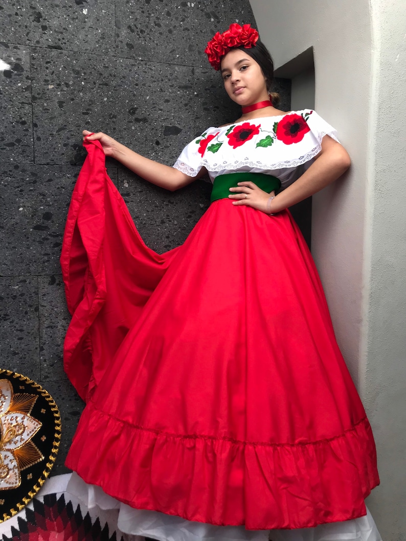 May include: A white off-the-shoulder blouse with red poppy floral embroidery and lace trim, paired with a wide green sash and a long, voluminous red skirt with a ruffled hem. A red floral headpiece and a red choker complete the ensemble.