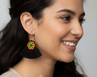 May include: Black tassel earrings with a beaded flower design in red, yellow, and green. The earrings are suspended from gold-colored hooks. The image also includes the text "MÉXICO TODO CORAZÓN".