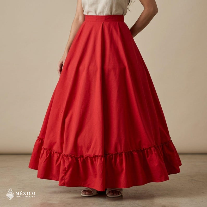 May include: A floor-length, solid red skirt featuring a high waistband and a wide, gathered ruffle along the bottom hem. The skirt has a full, voluminous silhouette and is paired with a plain, light-colored top. Text reads: M&Eacute;XICO TODO CORAZ&Oacute;N.
