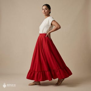 May include: A solid red ankle-length skirt featuring a gathered ruffle hemline, paired with a plain white short-sleeved top. The skirt has a high waistband and a full, flowing silhouette. The text "M&Eacute;XICO TODO CORAZ&Oacute;N" appears in the bottom corner.