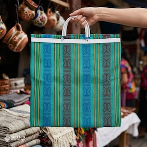May include: A turquoise and blue tote bag with a butterfly pattern and white handles. The bag has vertical stripes in shades of blue, green, and yellow. The bag is held by a person's hand.
